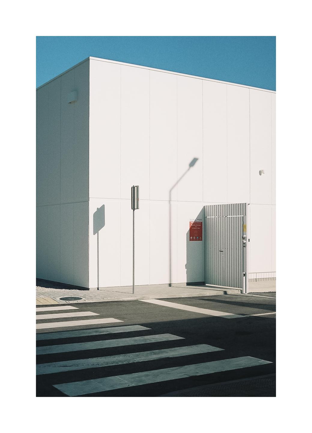 A white building with a gate and a street light stands next to a crosswalk under a clear blue sky.