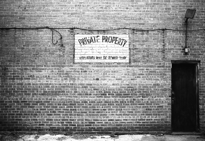 A brick wall features a "Private Property" sign, a light fixture, and a dark door.