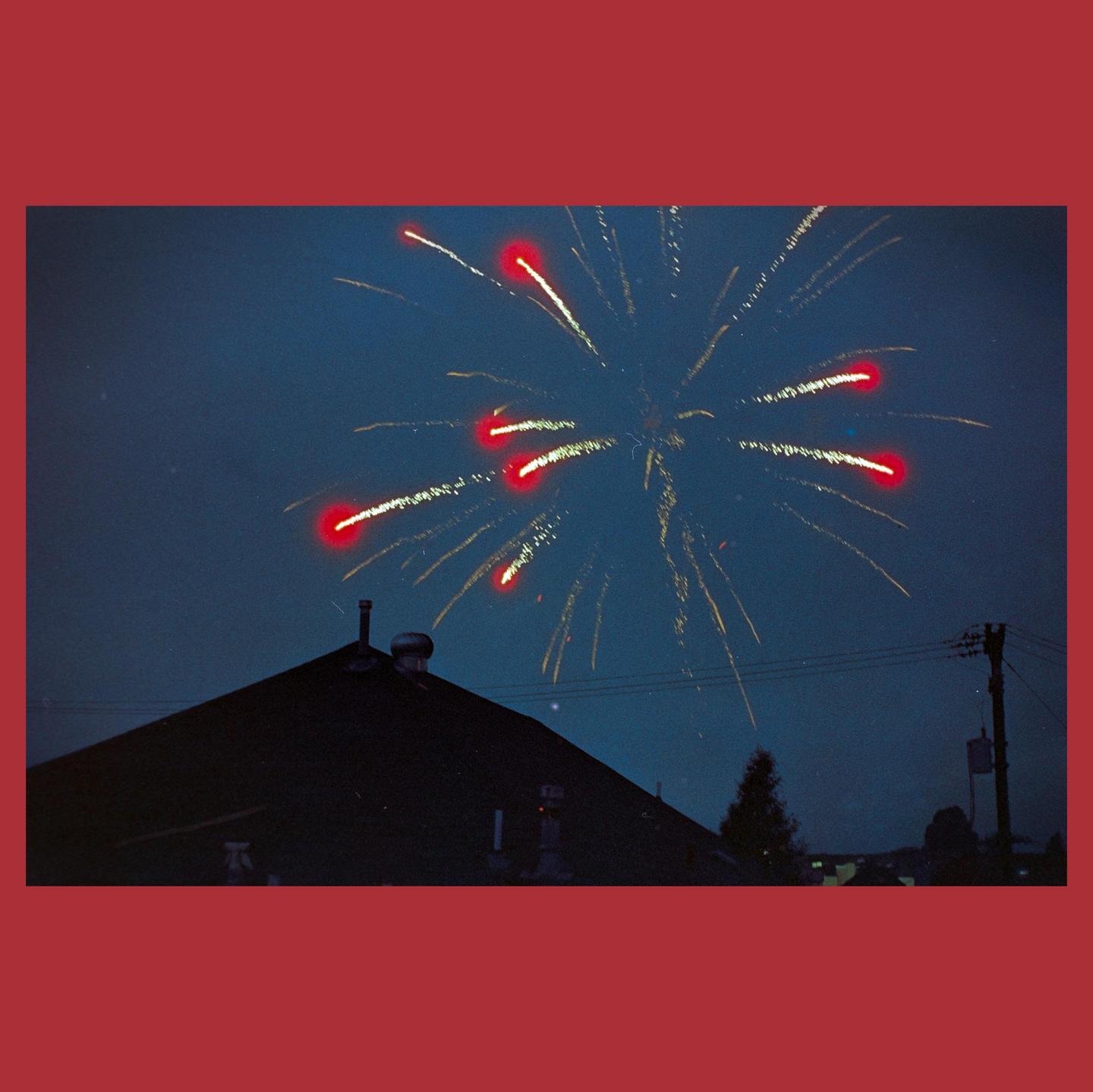 Fireworks explode in the night sky above a dark rooftop.