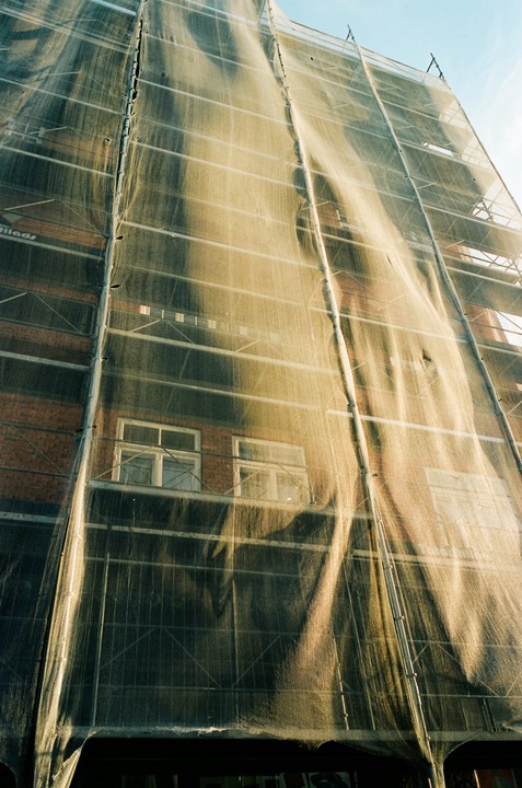 A building under construction is covered with scaffolding and a protective mesh.