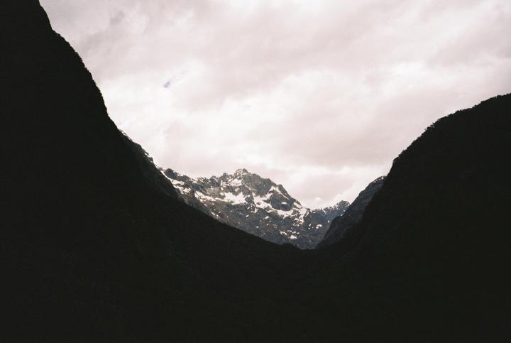 A snow-capped mountain peak is visible between two dark mountain slopes under a cloudy sky.