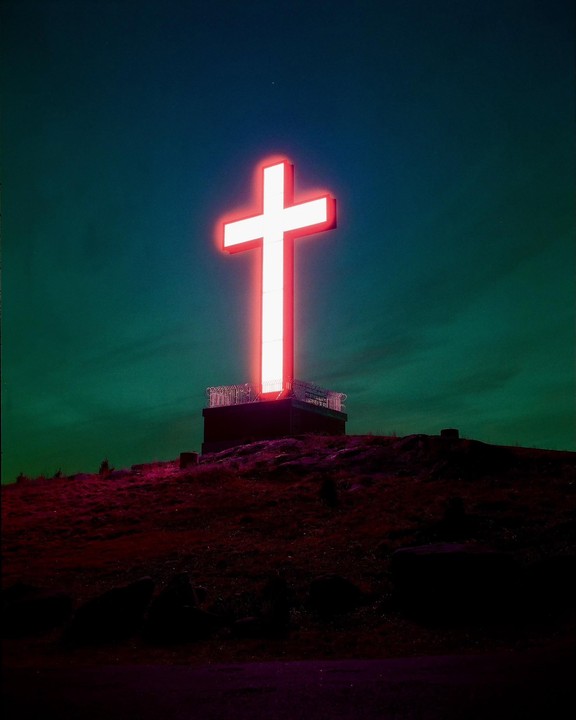 A large glowing red cross stands atop a hill against a dark sky.