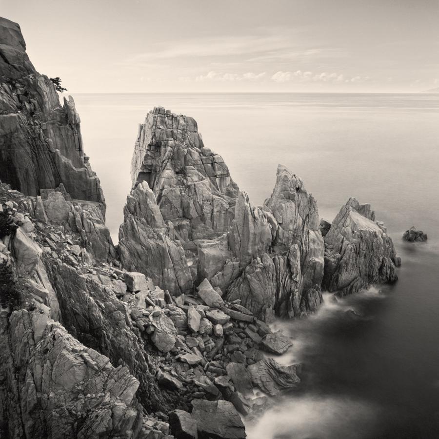 Jagged rock formations rise from the ocean under a cloudy sky.