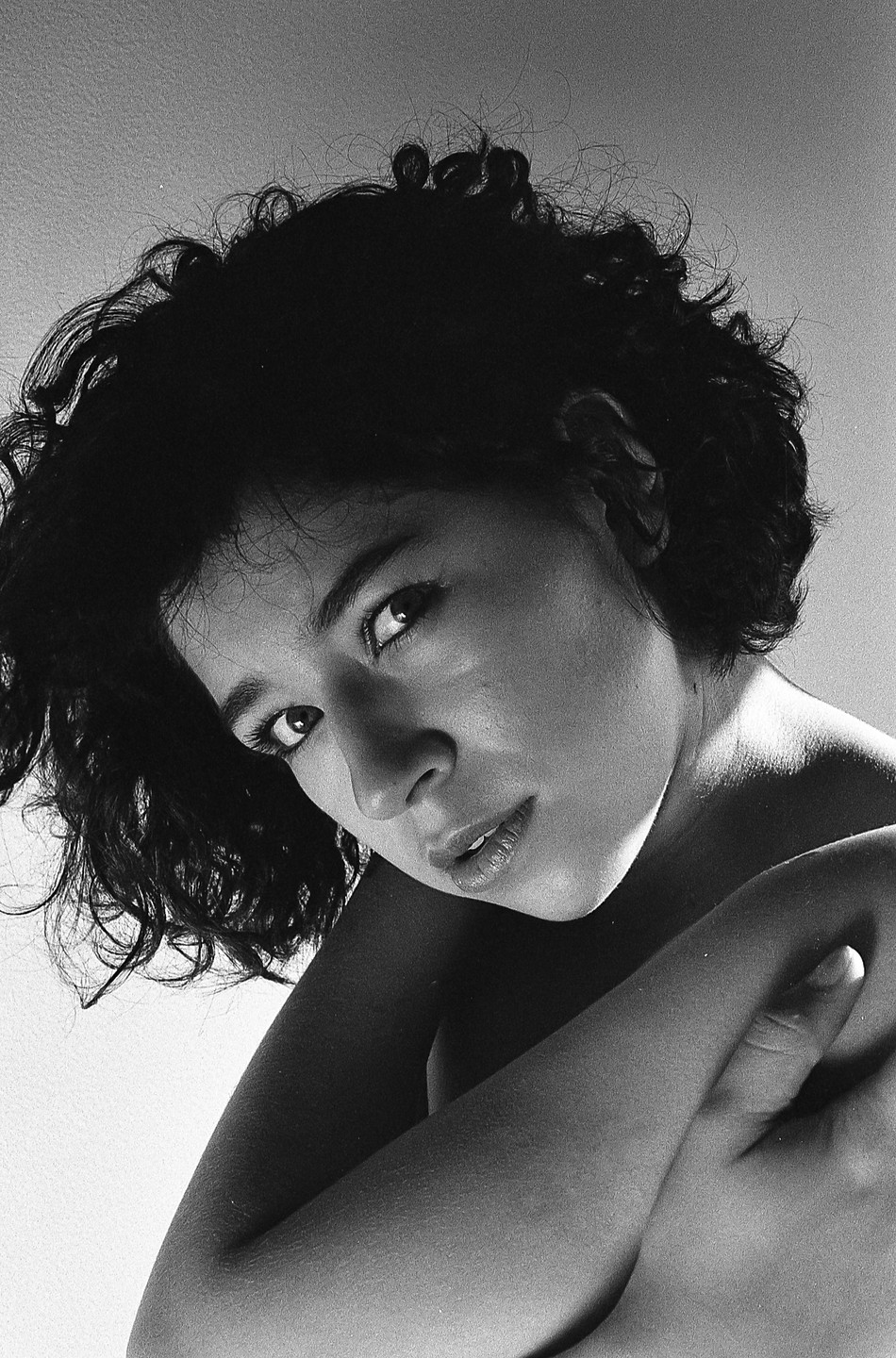 A woman with curly hair looks up at the viewer, with her arms crossed in front of her.