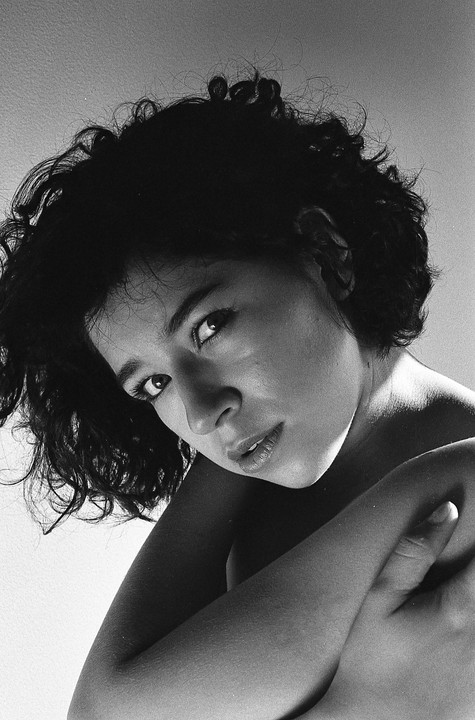A woman with curly hair looks up at the viewer, with her arms crossed in front of her.