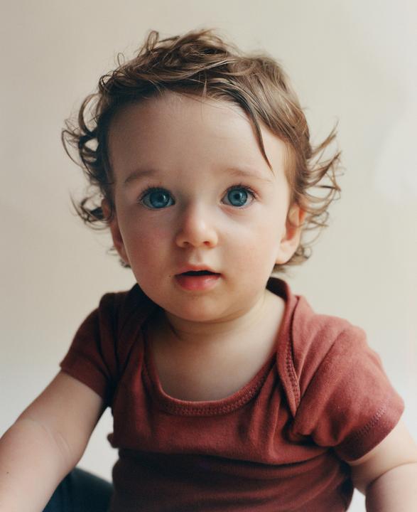 A baby with blue eyes and curly hair looks forward.