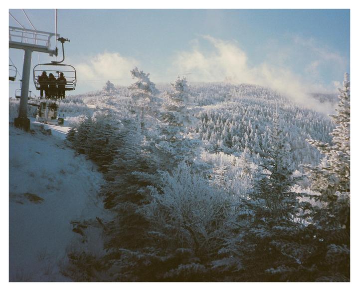A ski lift carries people over a snow-covered mountain with evergreen trees.