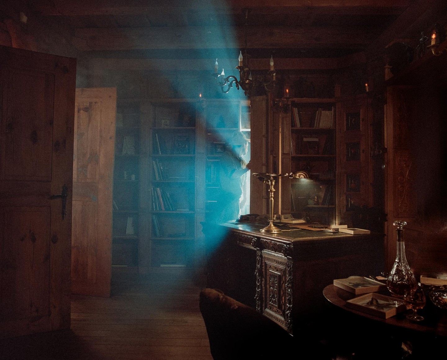 A beam of blue light illuminates a dark, wood-paneled room with bookshelves and a desk.