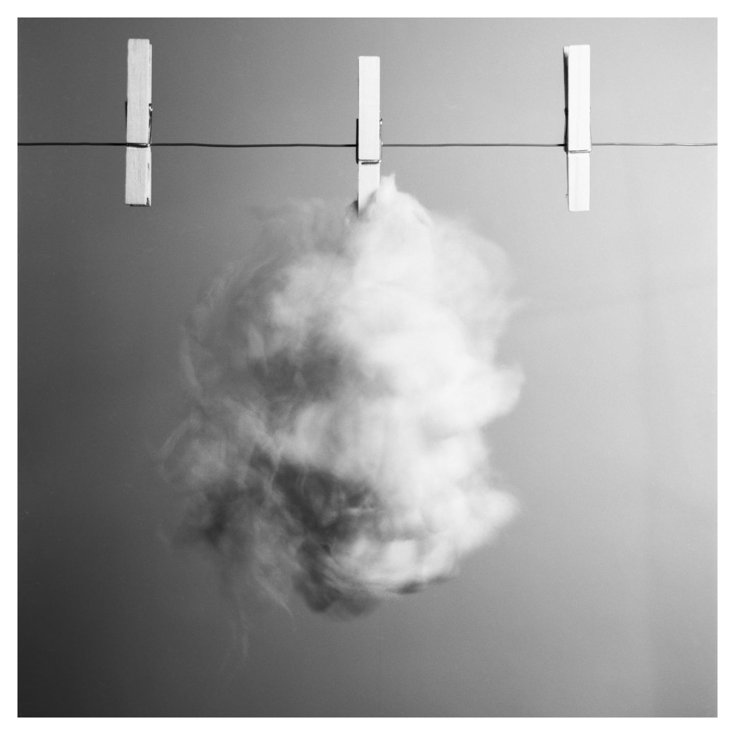 A cloud of smoke is suspended from a clothesline by three clothespins.