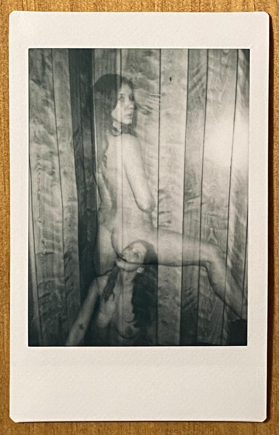 A double exposure shows a nude woman in two different poses against a wooden wall.