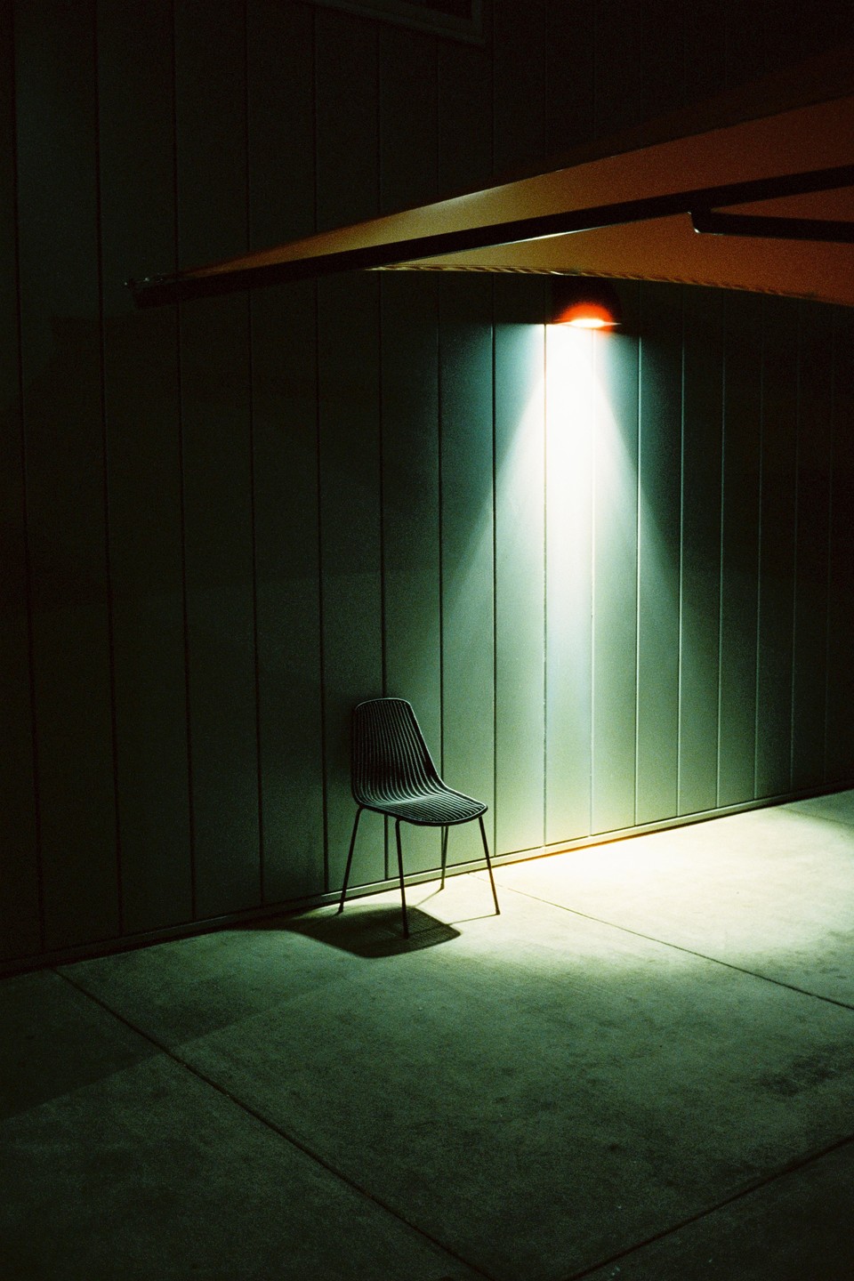 A single chair sits on a concrete floor illuminated by a spotlight against a paneled wall at night.