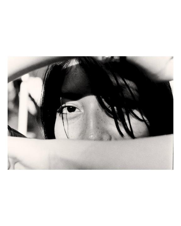 A woman's face is partially obscured by her arm and hair, with one eye looking directly at the viewer.