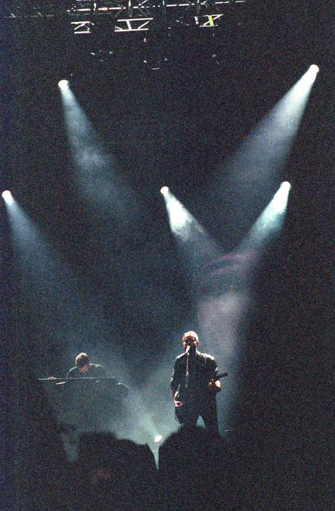 A band performs on a dark stage under bright spotlights.