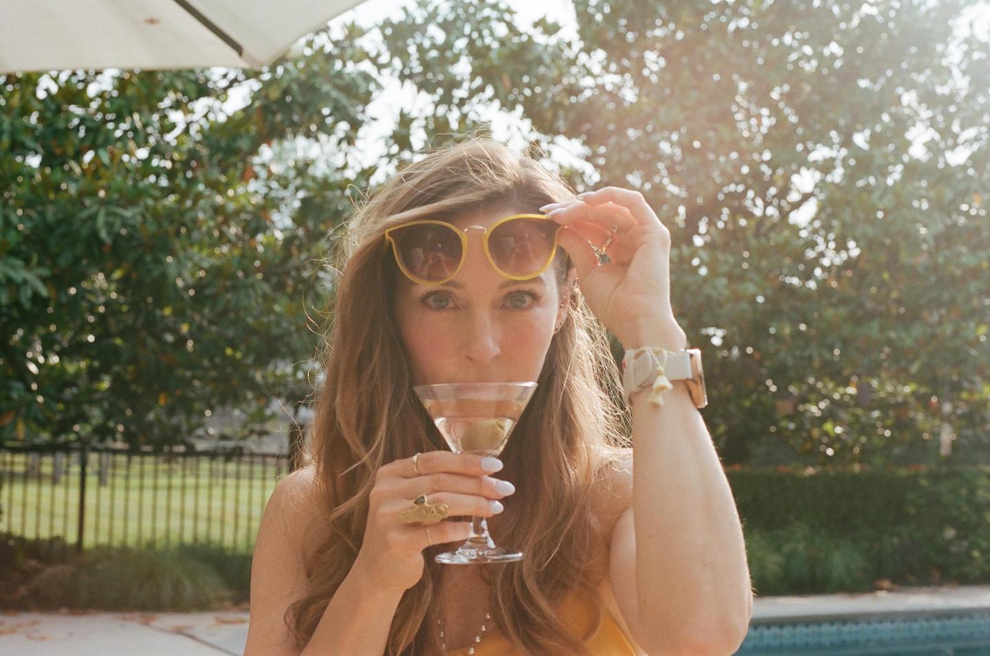 A woman sips a martini while holding her sunglasses up on her head.