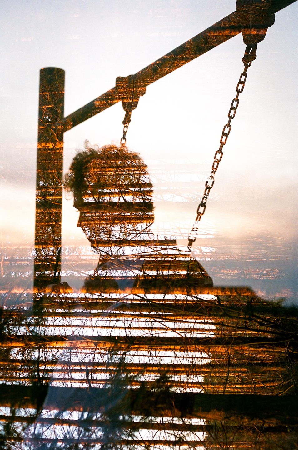 A double exposure shows a man's profile overlaid with a swing set and trees against a bright sky.