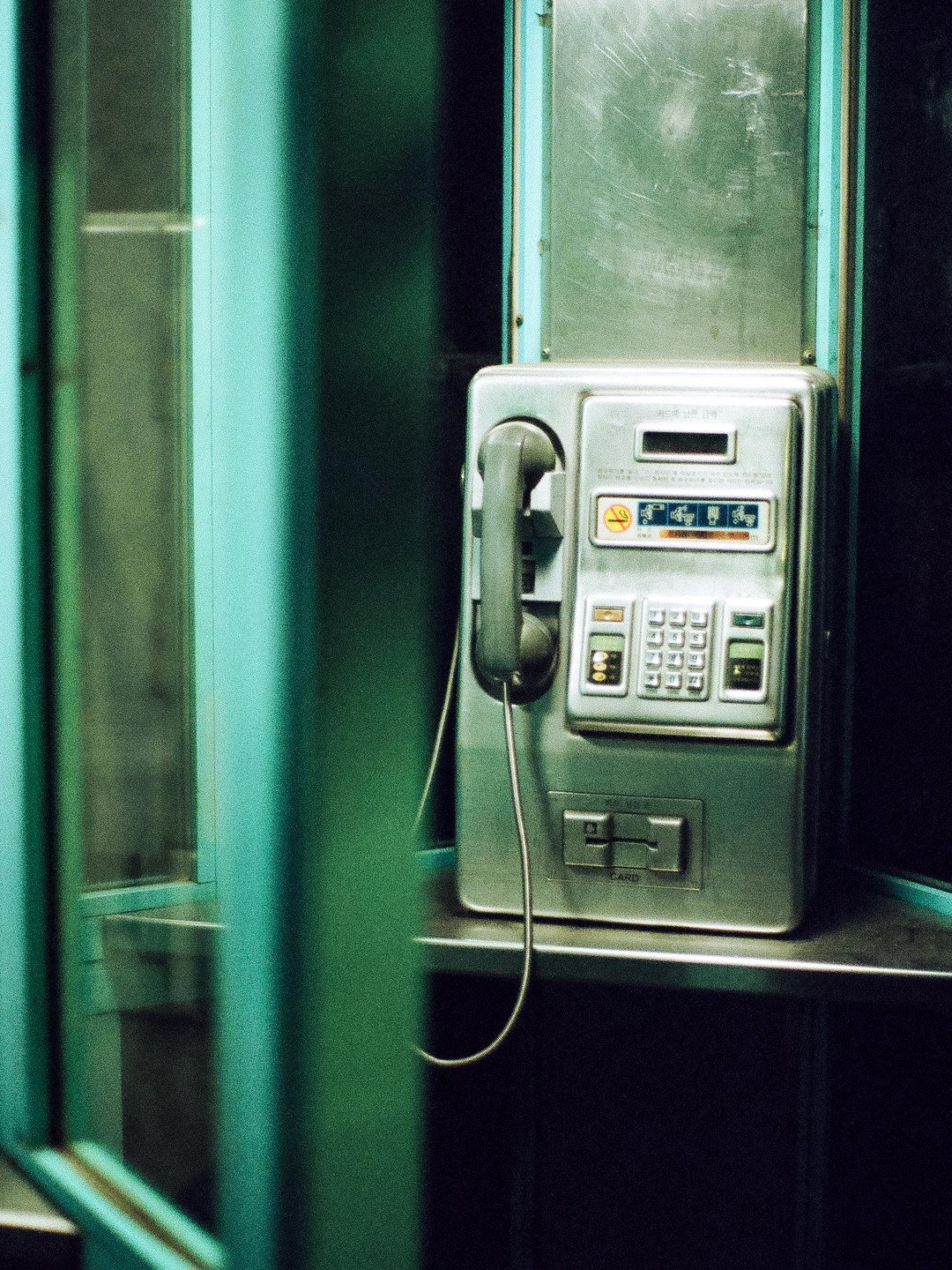 A payphone with a keypad and a card slot is visible inside a phone booth.