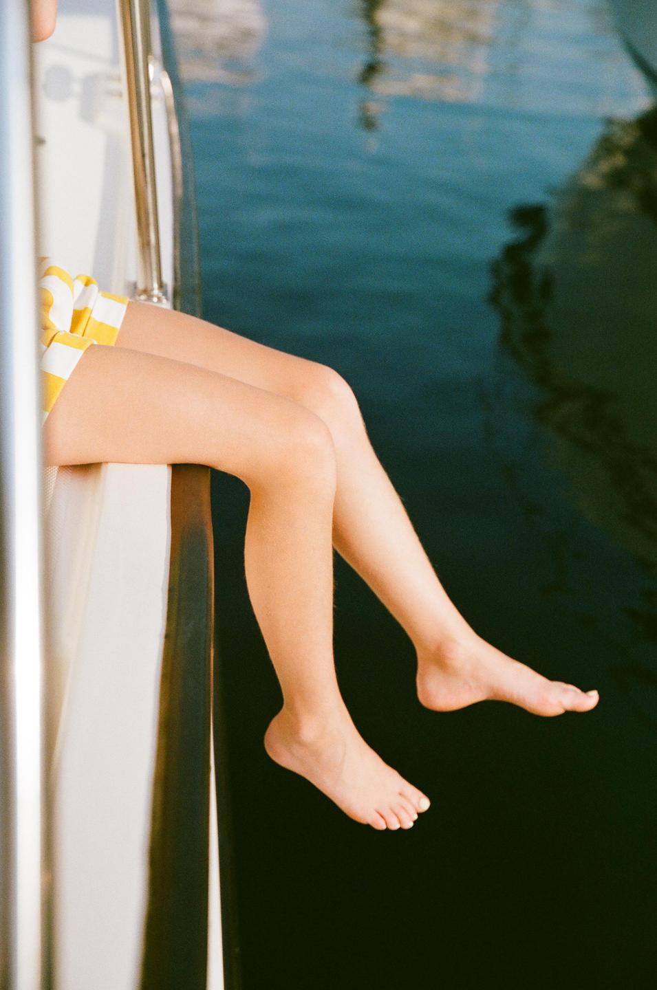 A person's legs dangle over the side of a boat with water below.