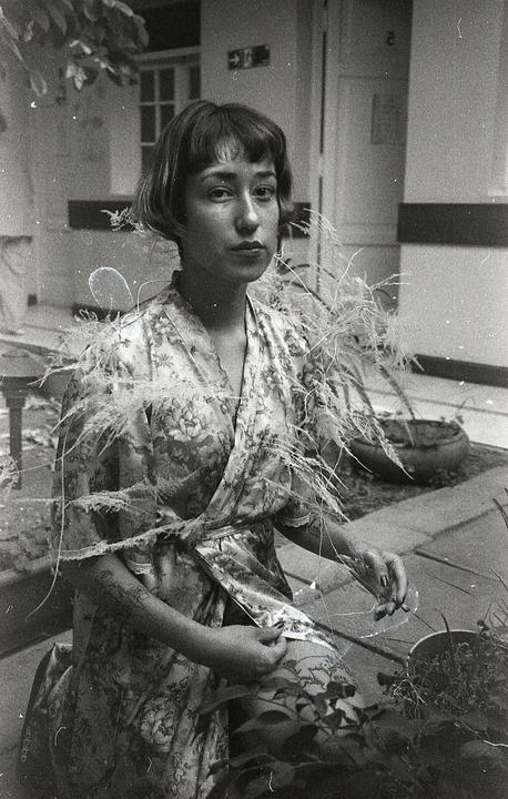 A woman in a floral robe with feathery adornments poses for a self-portrait.