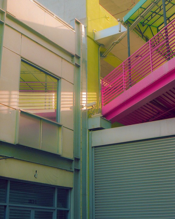 A bright pink staircase ascends a building with yellow walls and a metal facade.