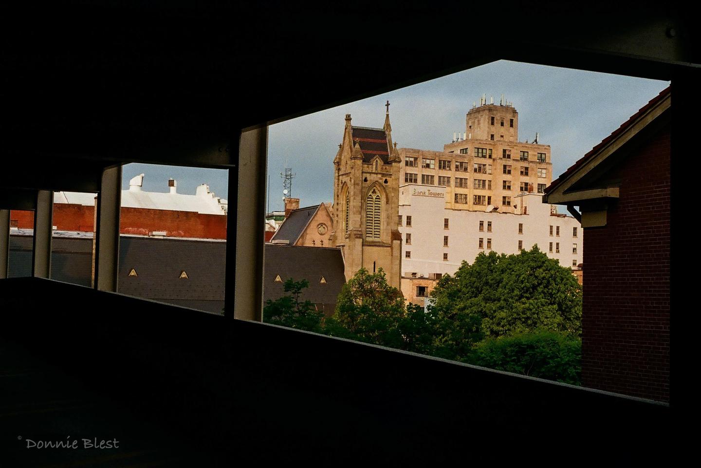 A church steeple and a tall building are visible through the dark, rectangular openings of a structure.