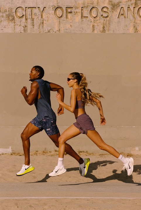 A man and a woman run side-by-side in front of a wall with "CITY OF LOS ANGELES" carved into it.