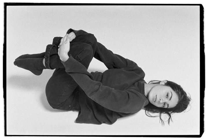 A woman lies on her back with her knees bent and her hands clasped around her shins.