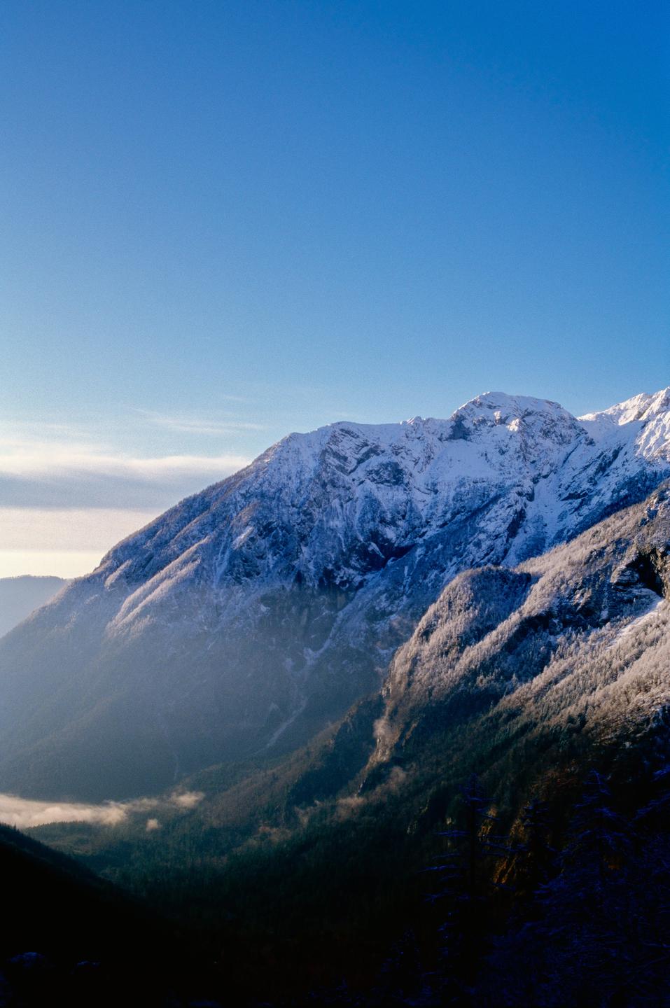 Snow-covered mountains rise above a valley with patches of fog.