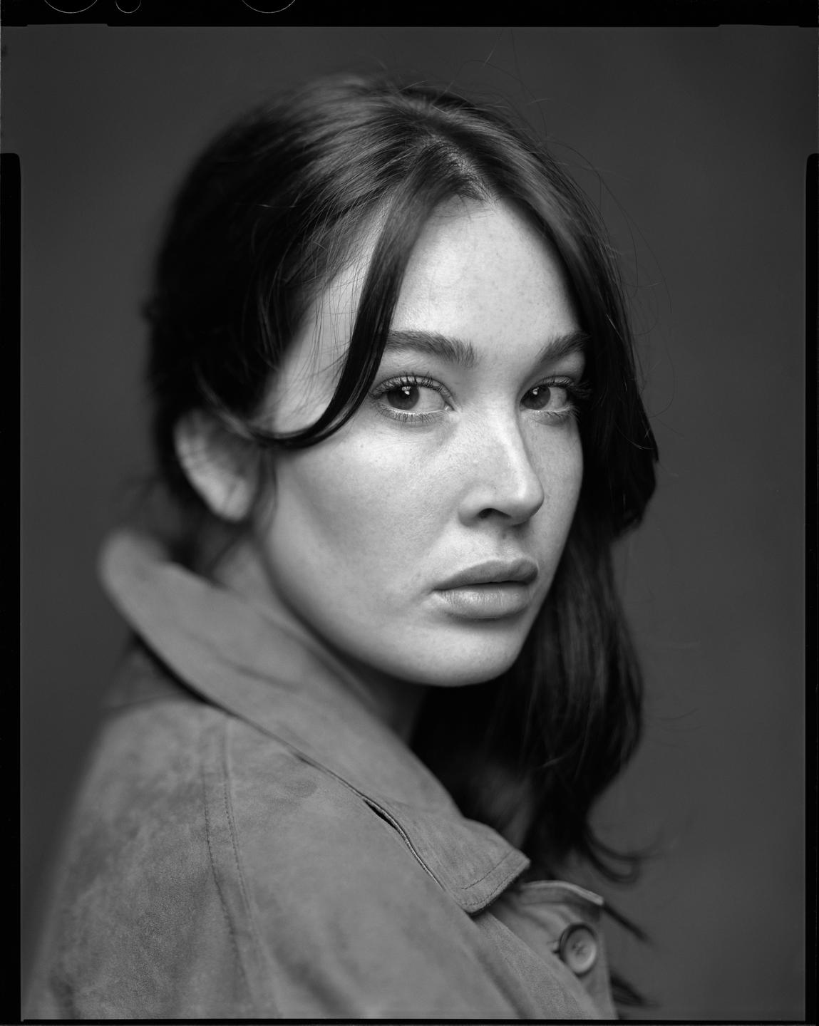 A woman with dark hair and a light-colored jacket looks directly at the viewer.
