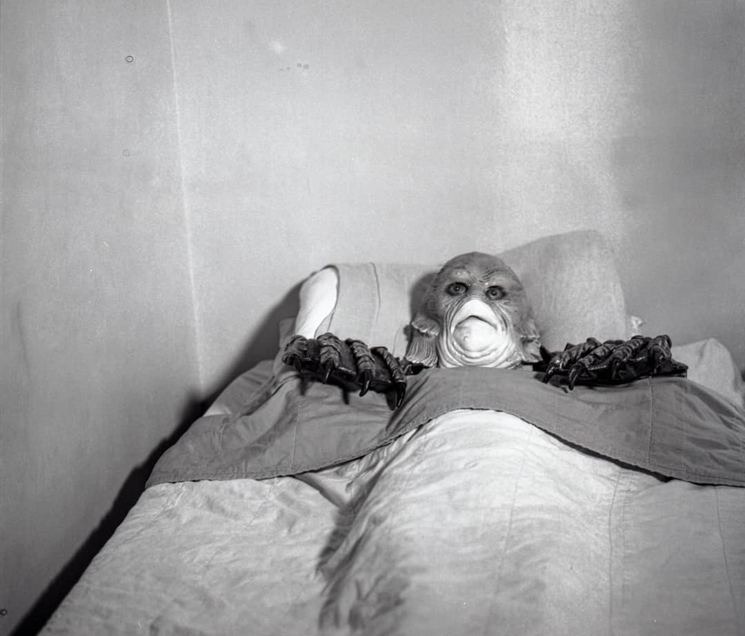A person in a monster costume with large claws lies in a bed.