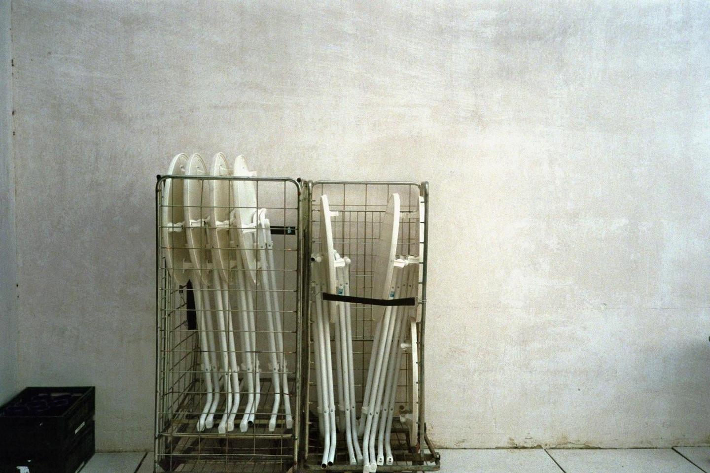 Two metal trolleys filled with white folding chairs stand against a textured white wall.