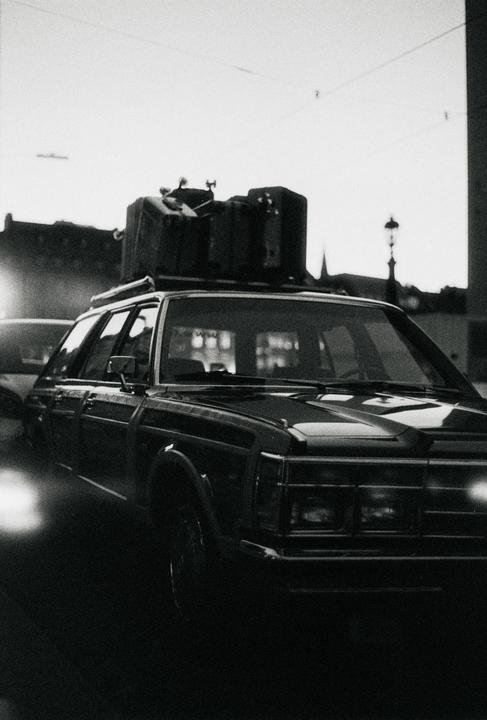A car with luggage on its roof rack is parked on a street at dusk.