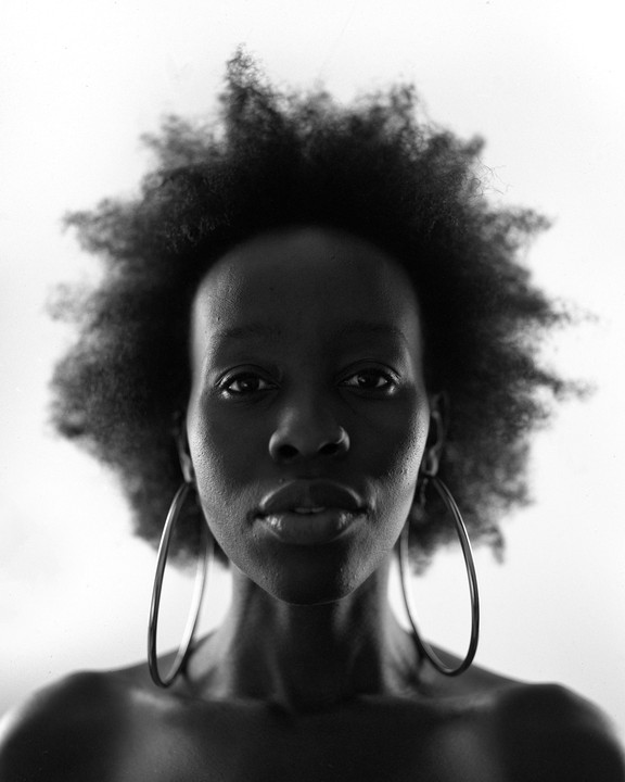 A woman with large hoop earrings and afro hair looks directly at the viewer.
