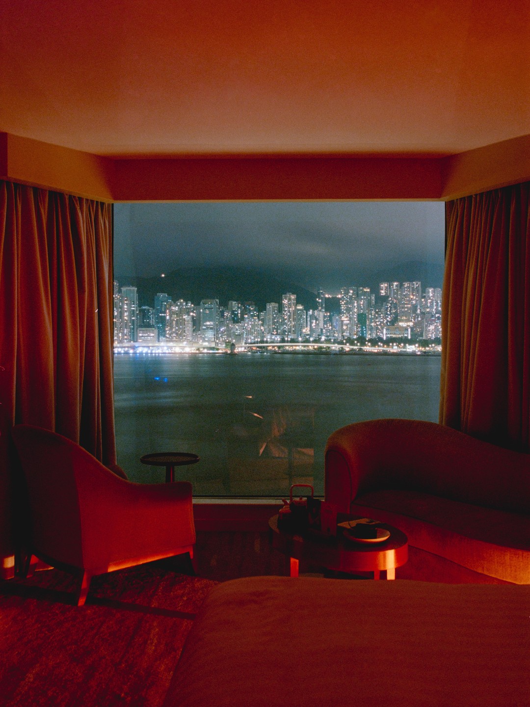 A hotel room with red lighting overlooks a city skyline at night.