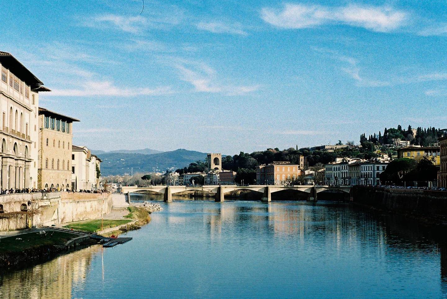 A river flows under a bridge with buildings and hills on both banks.