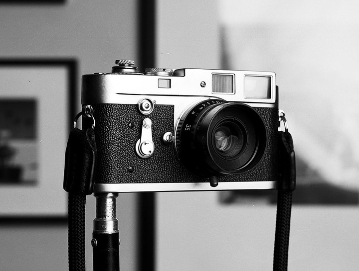 A camera with a lens and strap is mounted on a tripod.