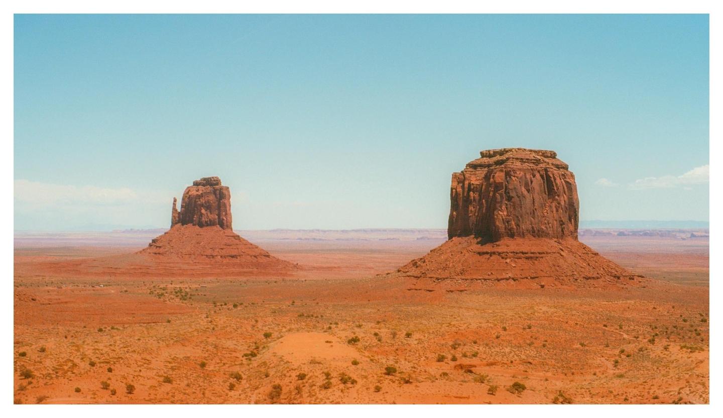 Two large rock formations stand in a vast desert landscape under a clear sky.