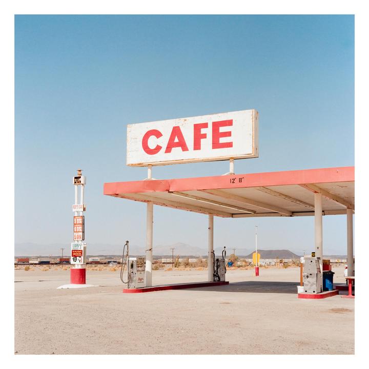 A cafe sign stands over a gas station in a desert landscape.
