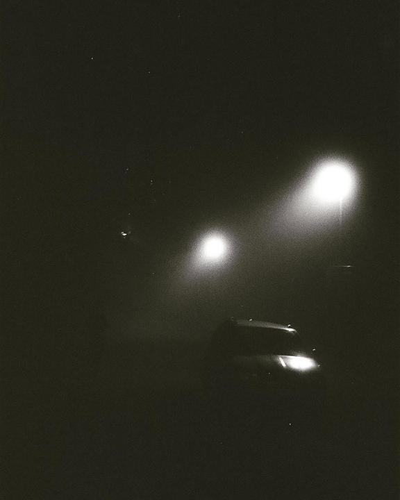 A car is visible in the dark with two bright lights in the background.