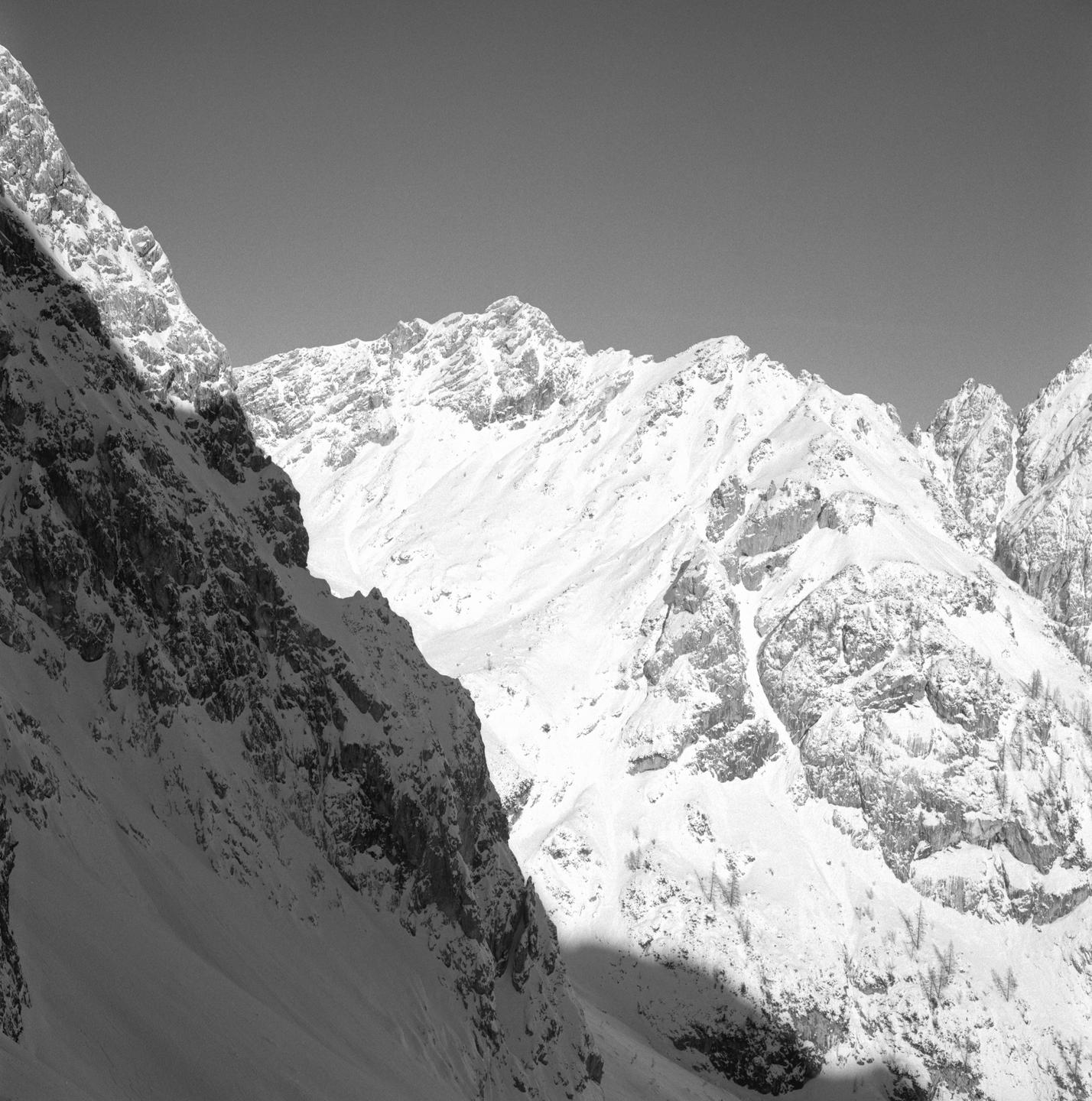 A black and white landscape shows snow-covered mountains under a clear sky.