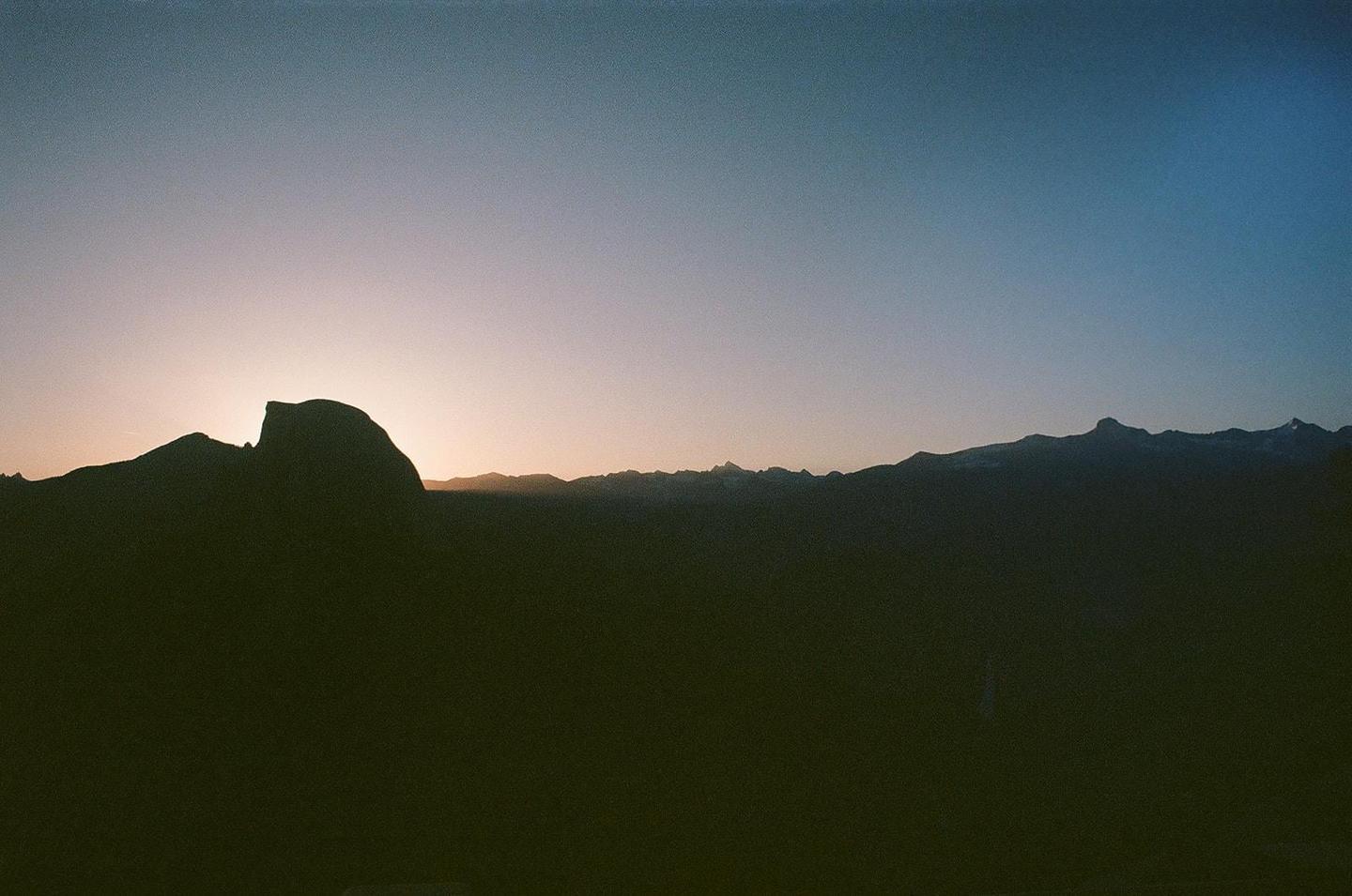 The sun rises behind a mountain range, silhouetting the peaks against a gradient sky.