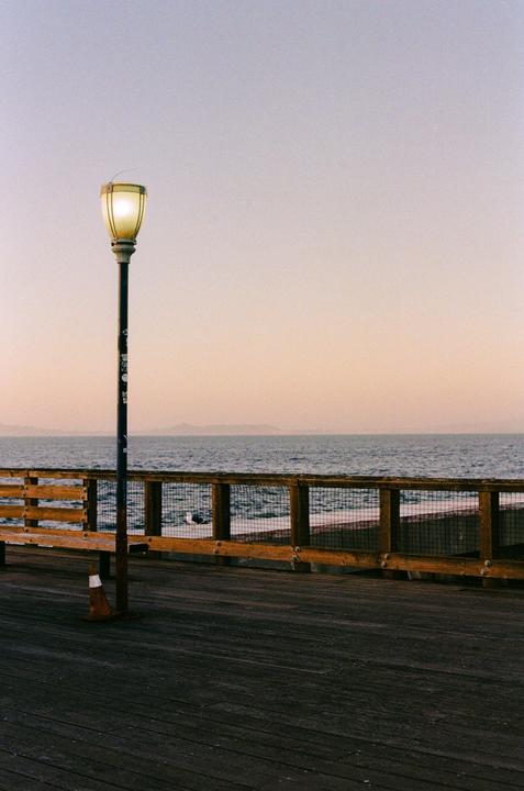 A street light illuminates a pier overlooking the ocean at dusk.