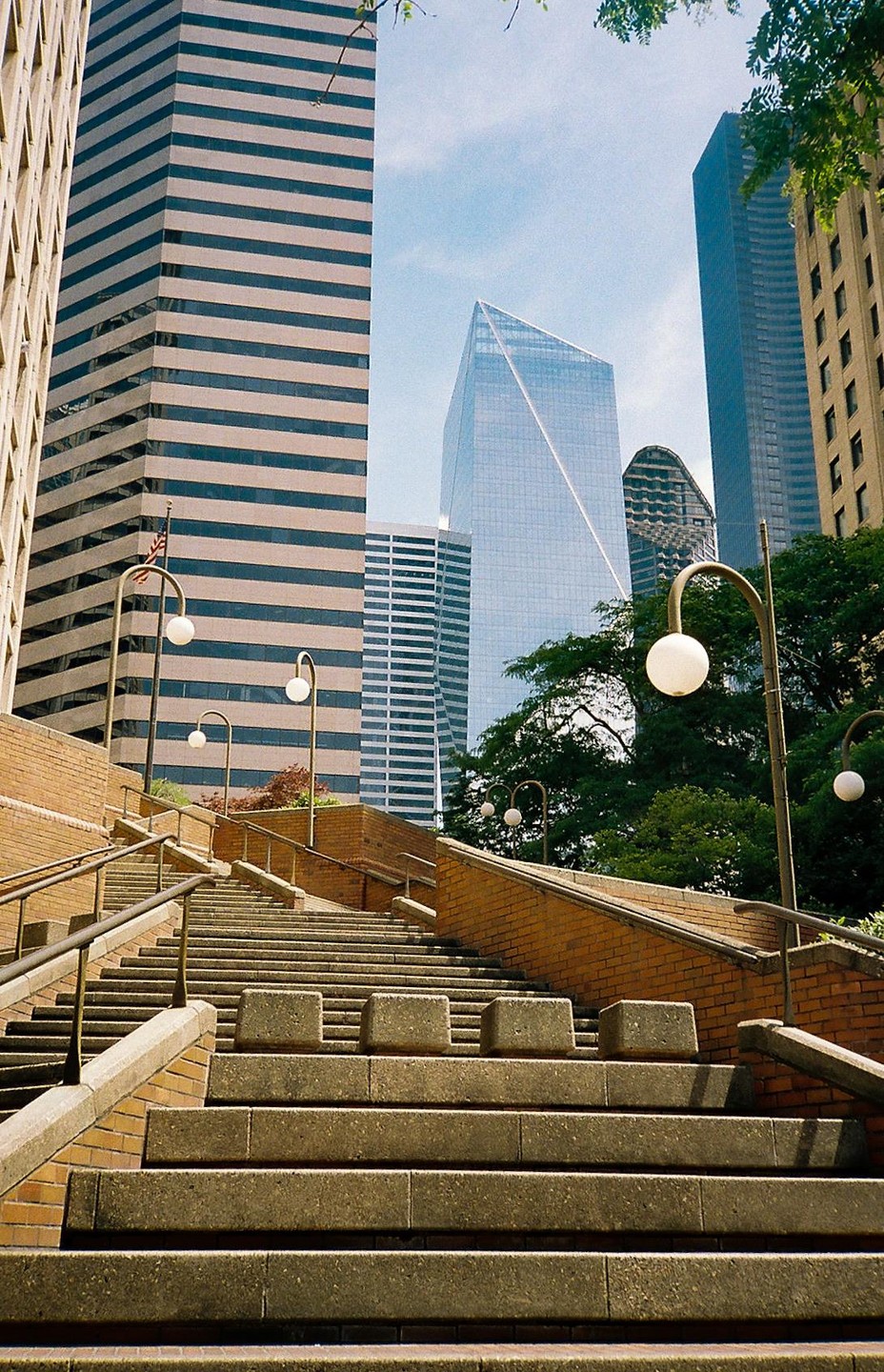 A long concrete staircase with brick walls and streetlights leads up to several tall buildings in a city.