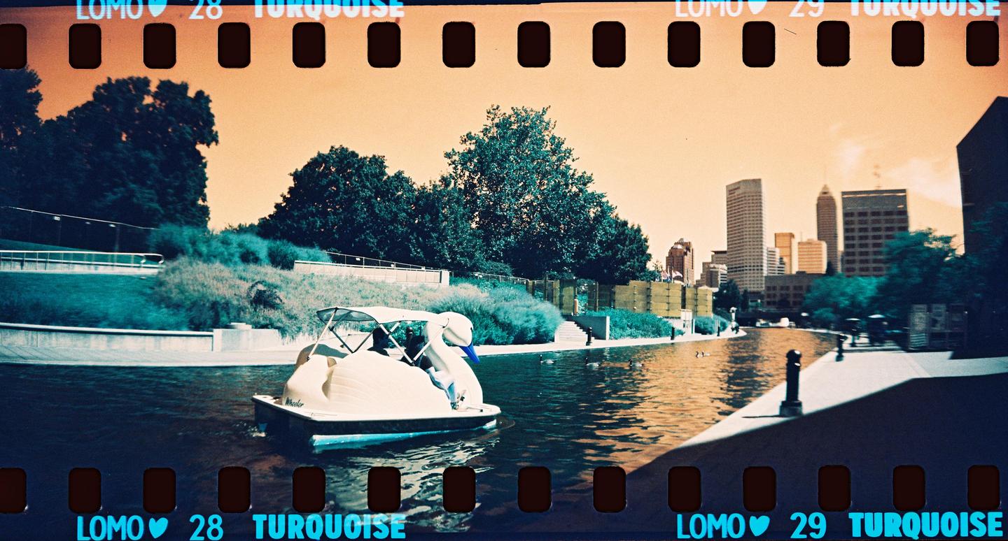 A swan pedal boat is on a canal with a city skyline in the background.