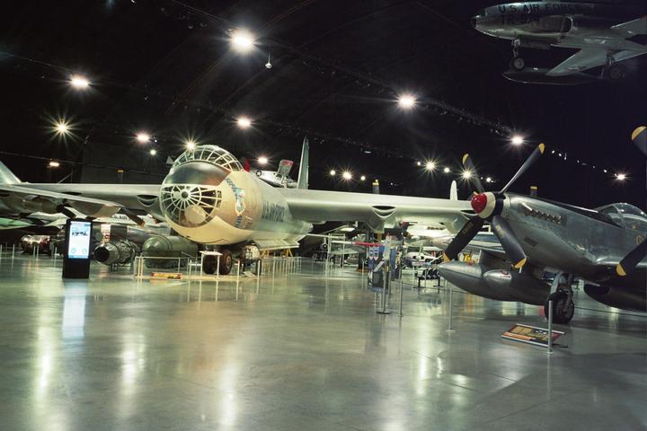 Several airplanes are displayed in a large, dimly lit hangar with bright lights on the ceiling.