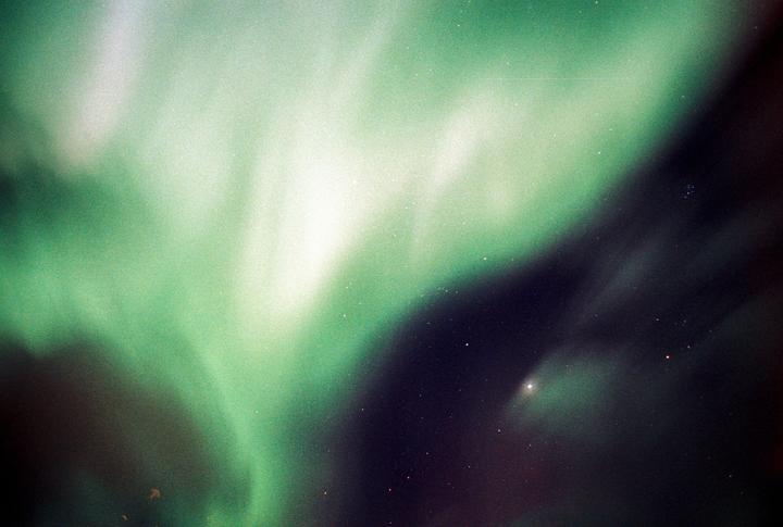 The northern lights glow green and white across a dark night sky filled with stars.