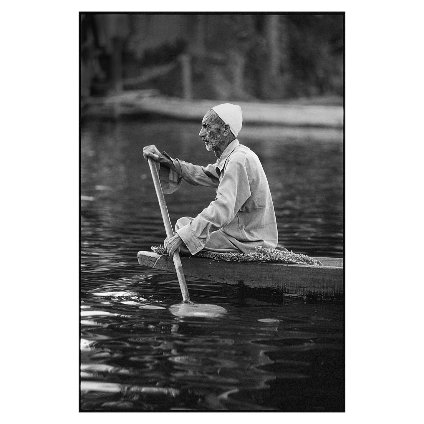 A man in a small boat paddles across a body of water.