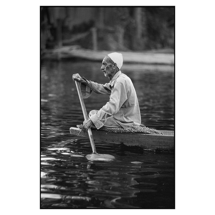 A man in a small boat paddles across a body of water.