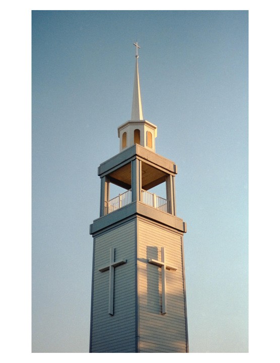 A church steeple with a cross on top and two crosses on its side stands against a clear sky.