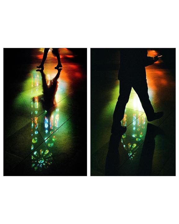 Two silhouettes of people are visible on a dark floor with colorful light patterns.