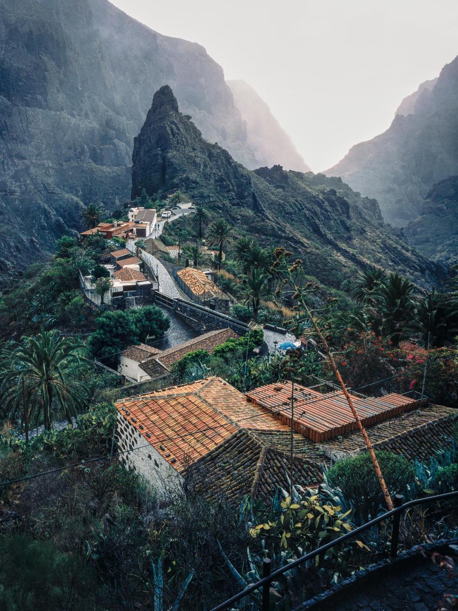 A small village with terracotta roofs is nestled in a valley between steep, rocky mountains.